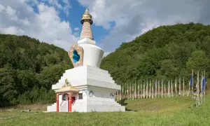 Biała stupa, miejsce, gdzie wyznaje się buddyzm, otoczona lasem i ozdobiona kolorowymi flagami modlitewnymi.