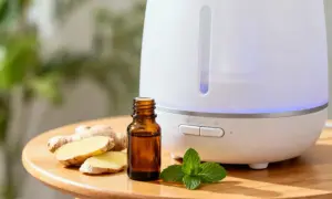 Biały dyfuzor z niebieskim podświetleniem, obok buteleczka olejku, imbir i listki mięty. Idealne do inhalacji.
