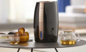 Elegancki czarny nawilżacz Philips z miedzianym akcentem. Obok szklanka z herbatą, bursztynowa buteleczka i mały dzbanuszek. Czy do każdego nawilżacza można wlać olejek?