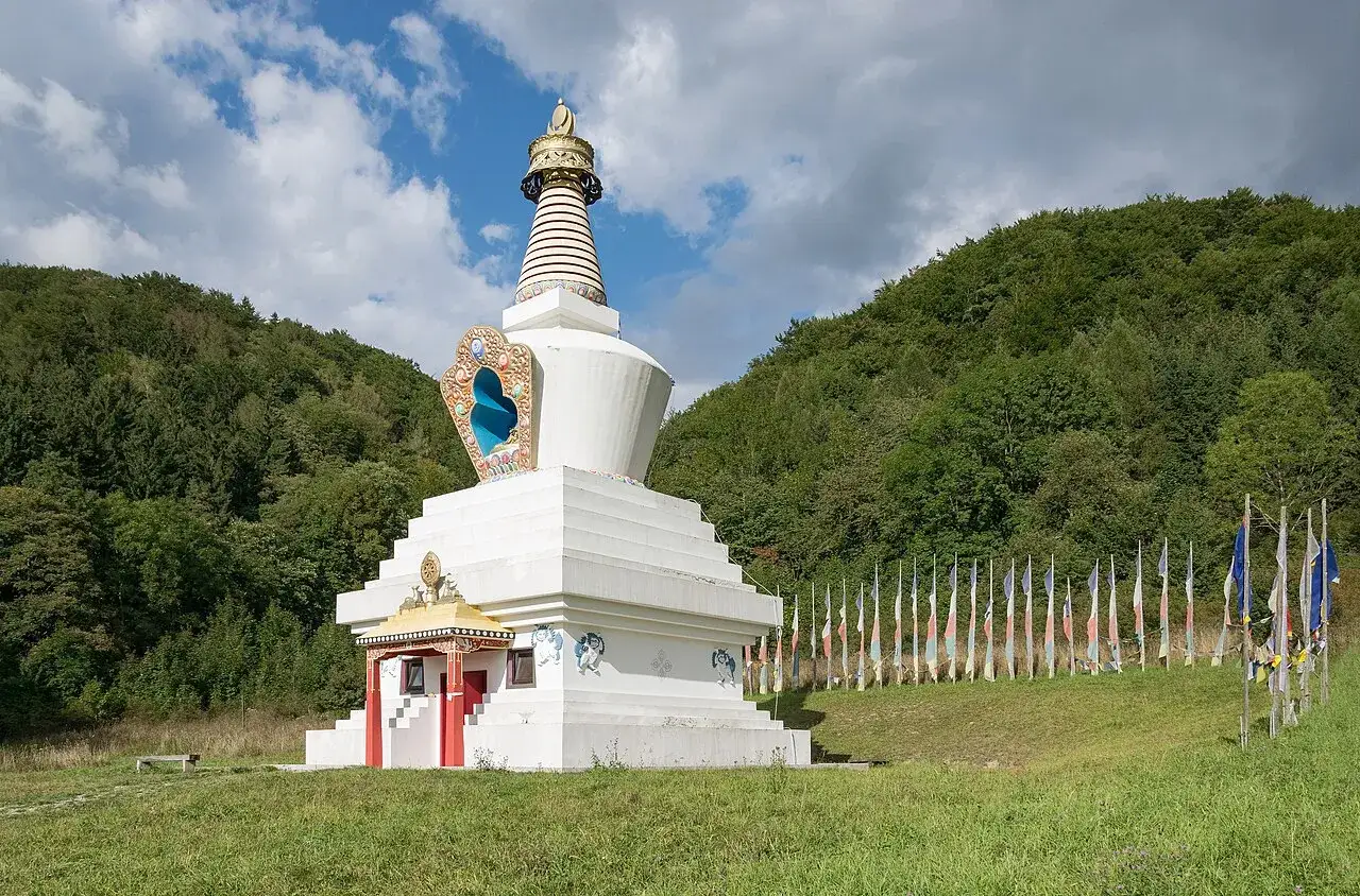Biała stupa, miejsce, gdzie wyznaje się buddyzm, otoczona lasem i flagami modlitewnymi.