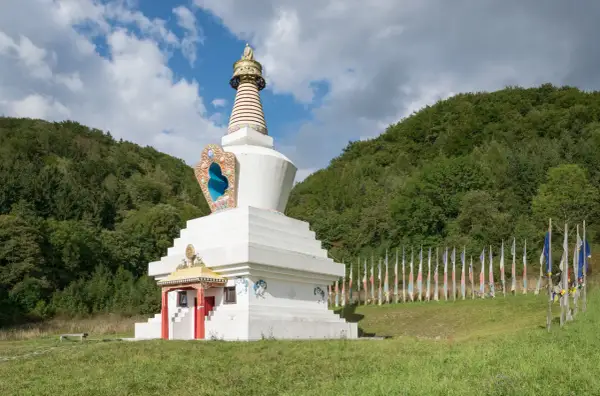 Biała stupa, miejsce, gdzie wyznaje się buddyzm, otoczona lasem i ozdobiona kolorowymi flagami modlitewnymi.